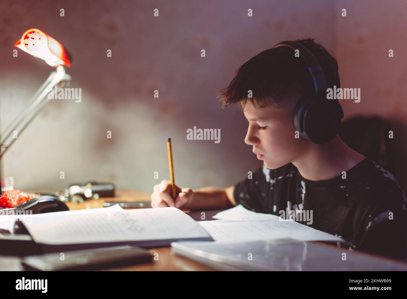 Piccolo ragazzo diligente che fa i compiti mentre ascolta la musica con le cuffie Foto Stock
