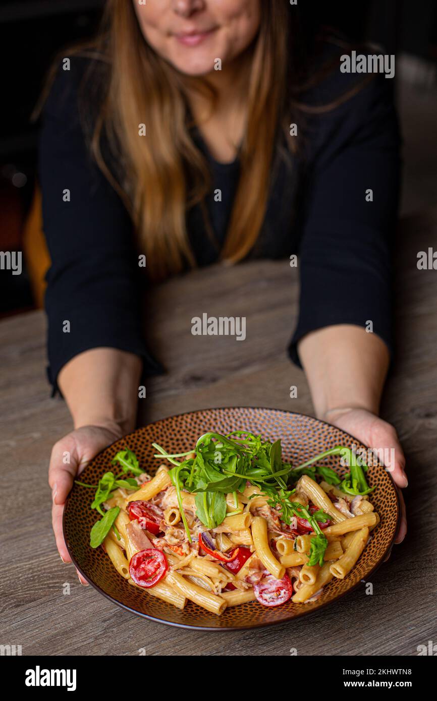 Donna verticale tagliata in vestito nero che tiene succosa, pronta a mangiare, pasta fresca biologica con basilico, salsa, carne, pomodoro Foto Stock