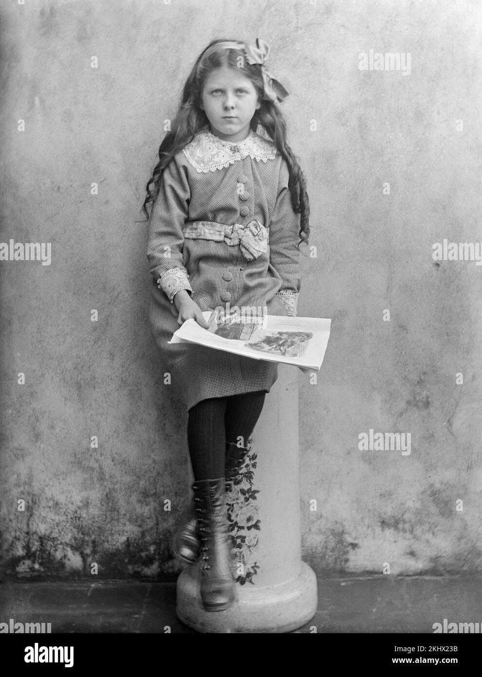 Una fotografia inglese vittoriana in bianco e nero di una giovane ragazza, molto seria, seduta su uno sgabello di pietra con un grande libro nelle sue mani. Foto Stock