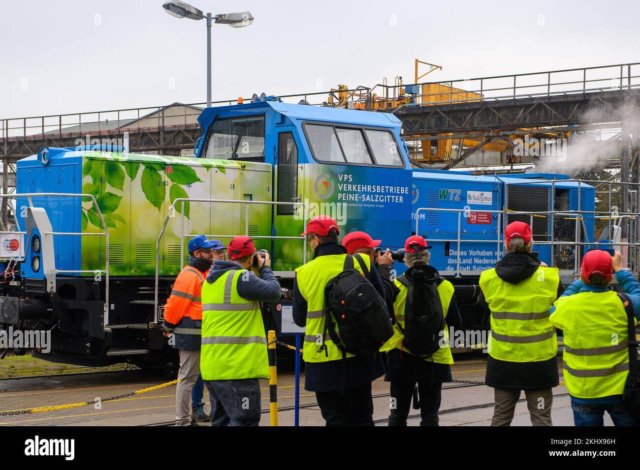 24 novembre 2022, Sassonia-Anhalt, Stendal: I rappresentanti dei media e i dipendenti di Alstom si trovano di fronte a una locomotiva di shunting alimentata a idrogeno, dalla quale il vapore sta crescendo. L'azienda vede un notevole potenziale nella conversione di locomotive shunting diesel in propulsione a idrogeno. In Germania, sono in funzione circa 1000 locomotive diesel shunting, e circa 4000 in tutta Europa. Fino ad ora, le locomotive ibride sono state azionate con una batteria e una trasmissione diesel; in futuro, saranno azionate con una batteria e una trasmissione a idrogeno. Una locomotiva emette circa 150 tonnellate di CO2 all'anno Foto Stock