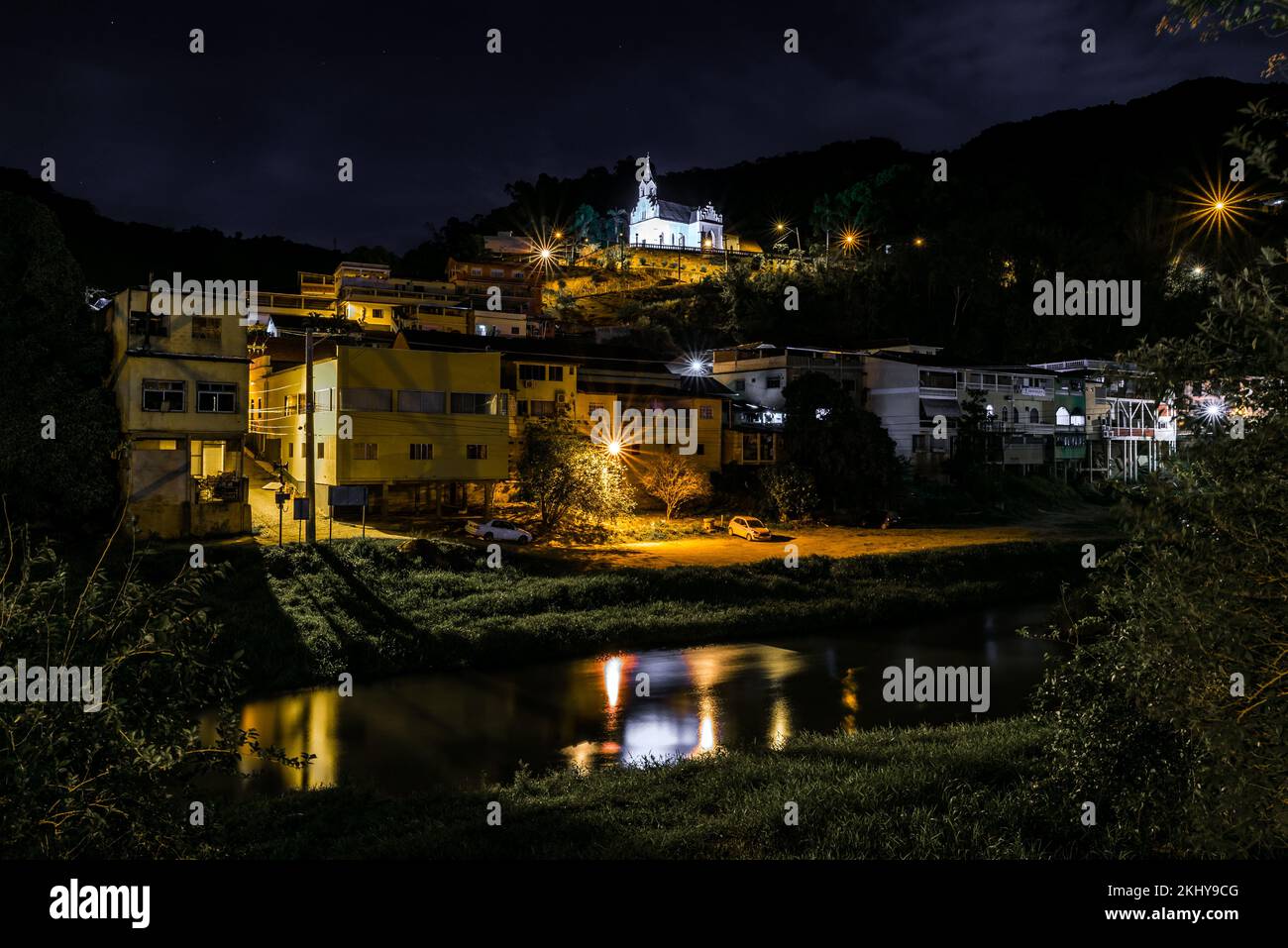 Notte Vista di case di fronte a un fiume e una Chiesa sulla collina nella città di Santa Leopoldina in Brasile Foto Stock