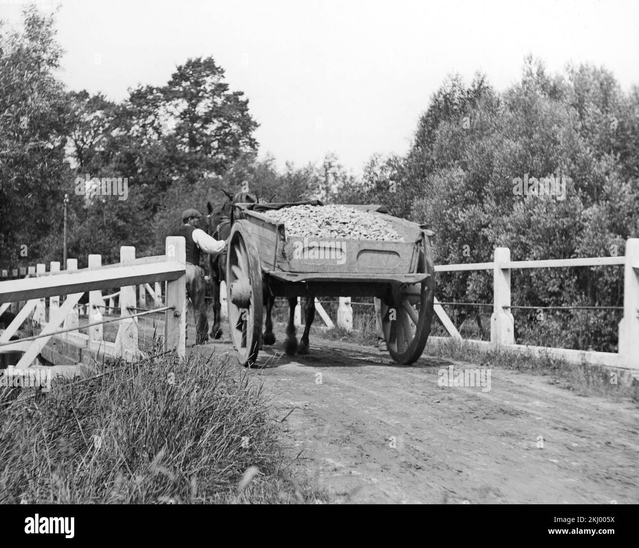 Una fotografia inglese in bianco e nero dei primi anni del 20th° secolo che mostra un contadino che guida un cavallo e un carro carico di prodotti. Foto Stock
