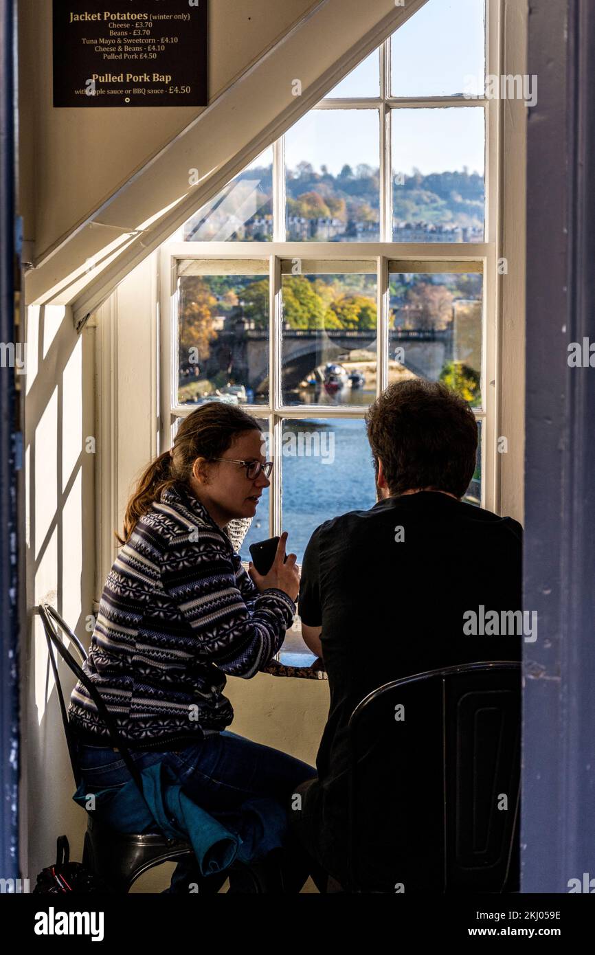 Una coppia chiacchiera mentre beve un caffè al Pulteney Bridge Coffee Shop a Bath Spa, Somerset, Inghilterra, Regno Unito Foto Stock