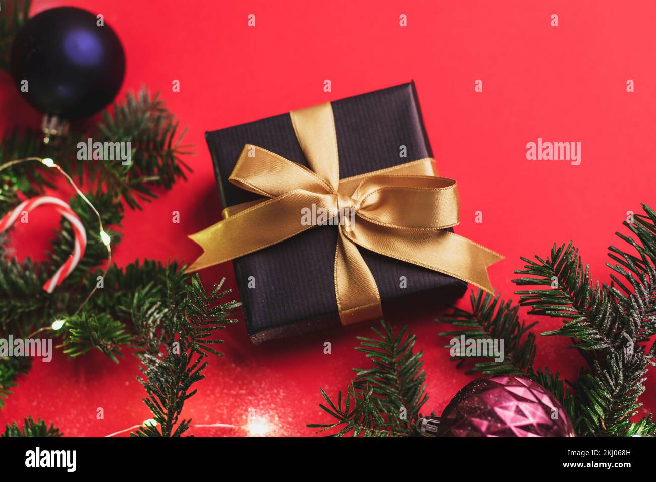 Scatola regalo nera con arco dorato, palline di Natale colorate e rami di abete con decorazioni natalizie su sfondo rosso. Concetto di vacanza invernale. Parte superiore v Foto Stock