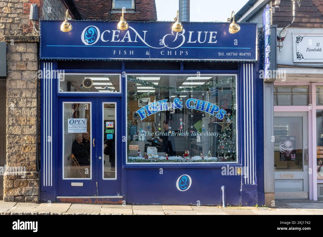 Ristorante tradizionale da asporto con piatti a base di pesce e patatine chiamato Ocean Blue nel centro di Midhurst, West Sussex, Inghilterra, Regno Unito, con i clienti in attesa all'interno Foto Stock