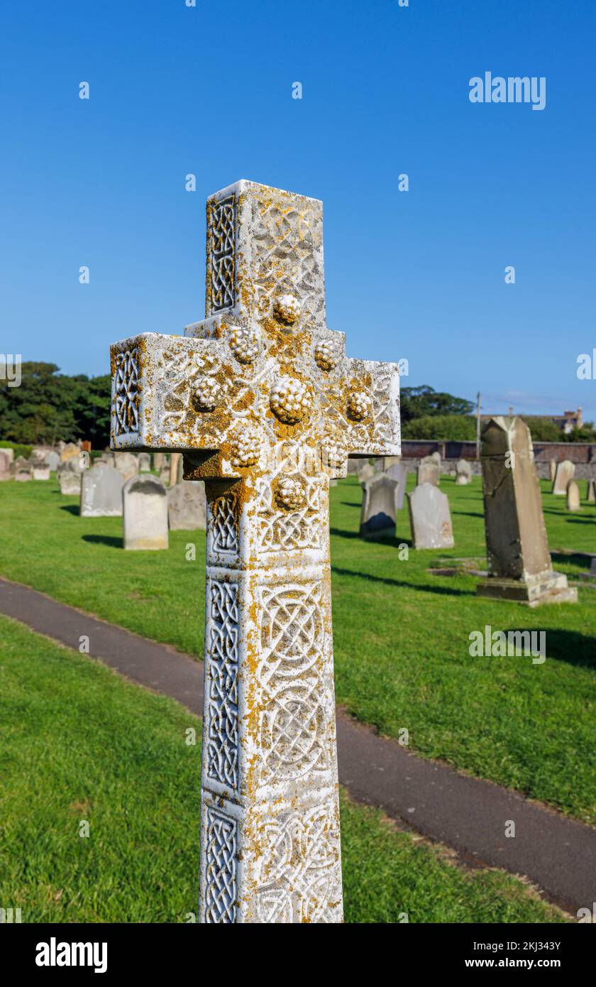 Croce commemorativa in pietra arrugginita di lichen nella chiesa di St Aidan a Bambburgh, un villaggio nel Northumberland sulla costa nord-orientale dell'Inghilterra Foto Stock