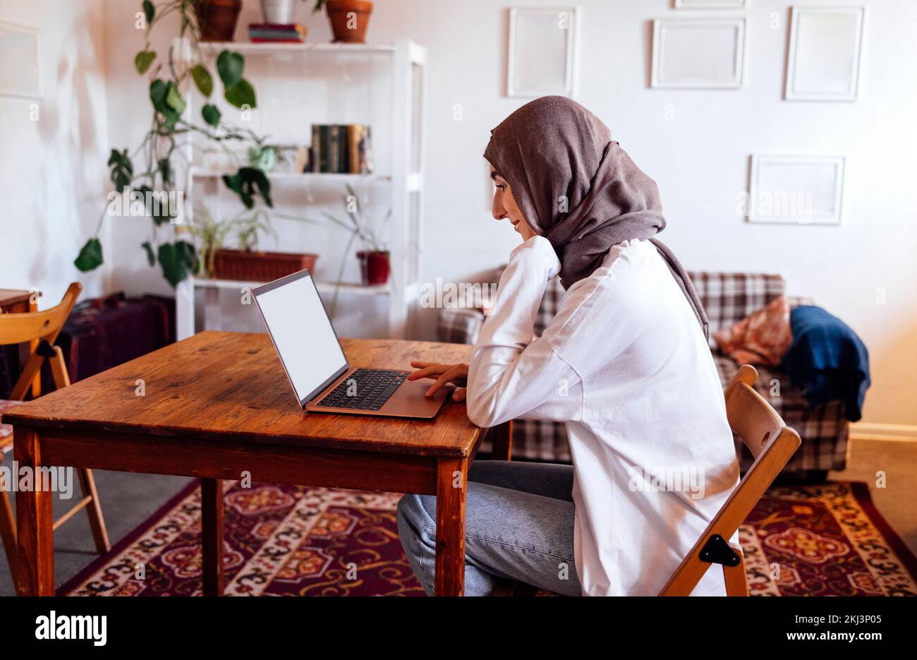 Giovane donna mediorientale che indossa un hijab usando un notebook a casa. Ragazza musulmana che si prepara per gli esami di ingresso. Istruzione domestica e concetto in linea di studio Foto Stock