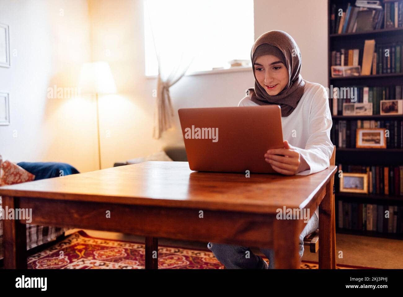 Giovane donna mediorientale che indossa un hijab usando un notebook a casa. Ragazza musulmana che si prepara per gli esami di ingresso. Istruzione domestica e concetto in linea di studio Foto Stock