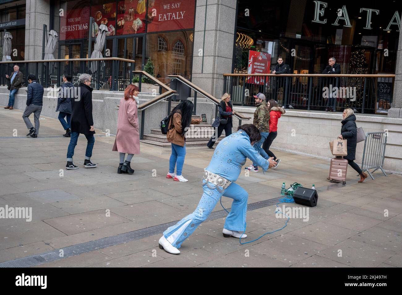 Il 24th novembre 2022, a Londra, in Inghilterra, un atto di tributo simile a quello di Elvis Presley rappresenta il Re davanti al passaggio di pendolari alla stazione di Liverpool Street nella City of London, il quartiere finanziario della capitale. Foto Stock
