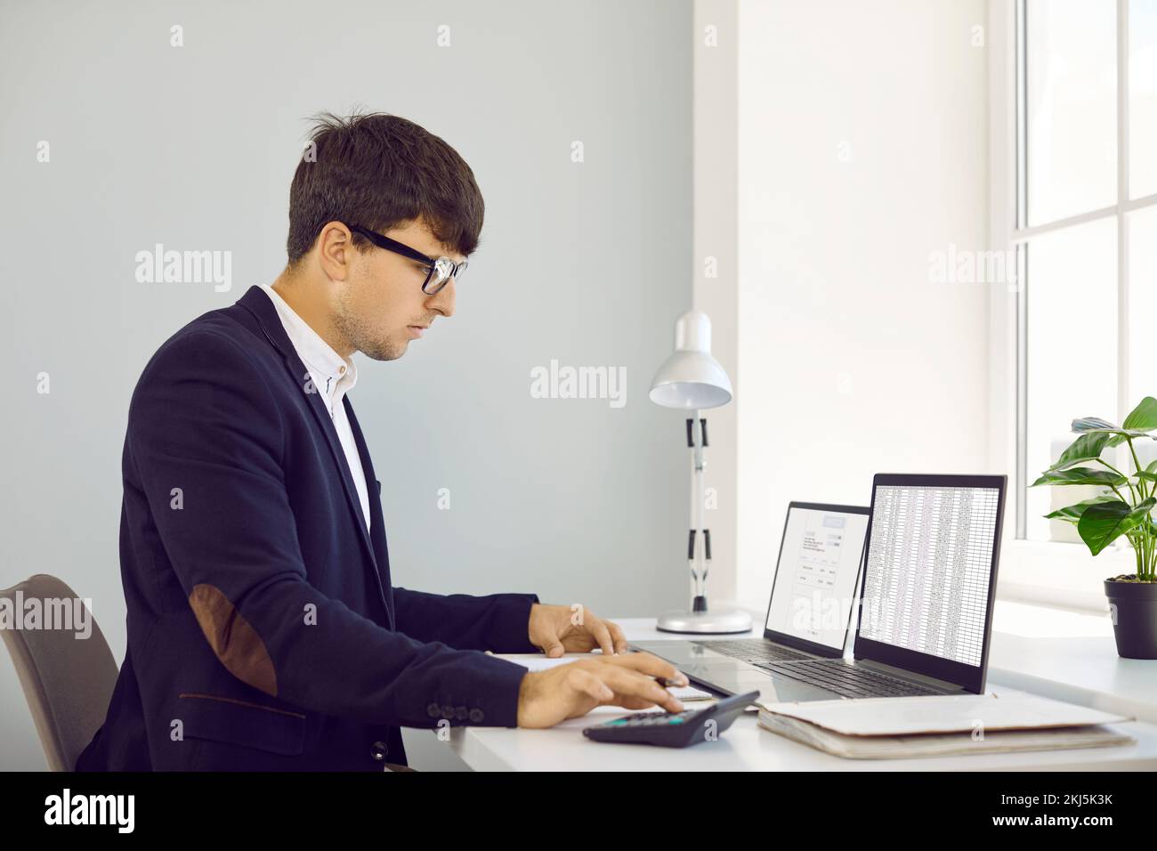 Contabile che utilizza la calcolatrice e lavora con documenti aziendali digitali sui computer portatili Foto Stock