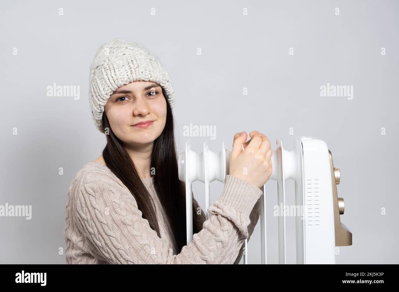 Una donna brunetta in un cappello abbraccia un riscaldatore, si riscalda in inverno, un posto per il testo Foto Stock