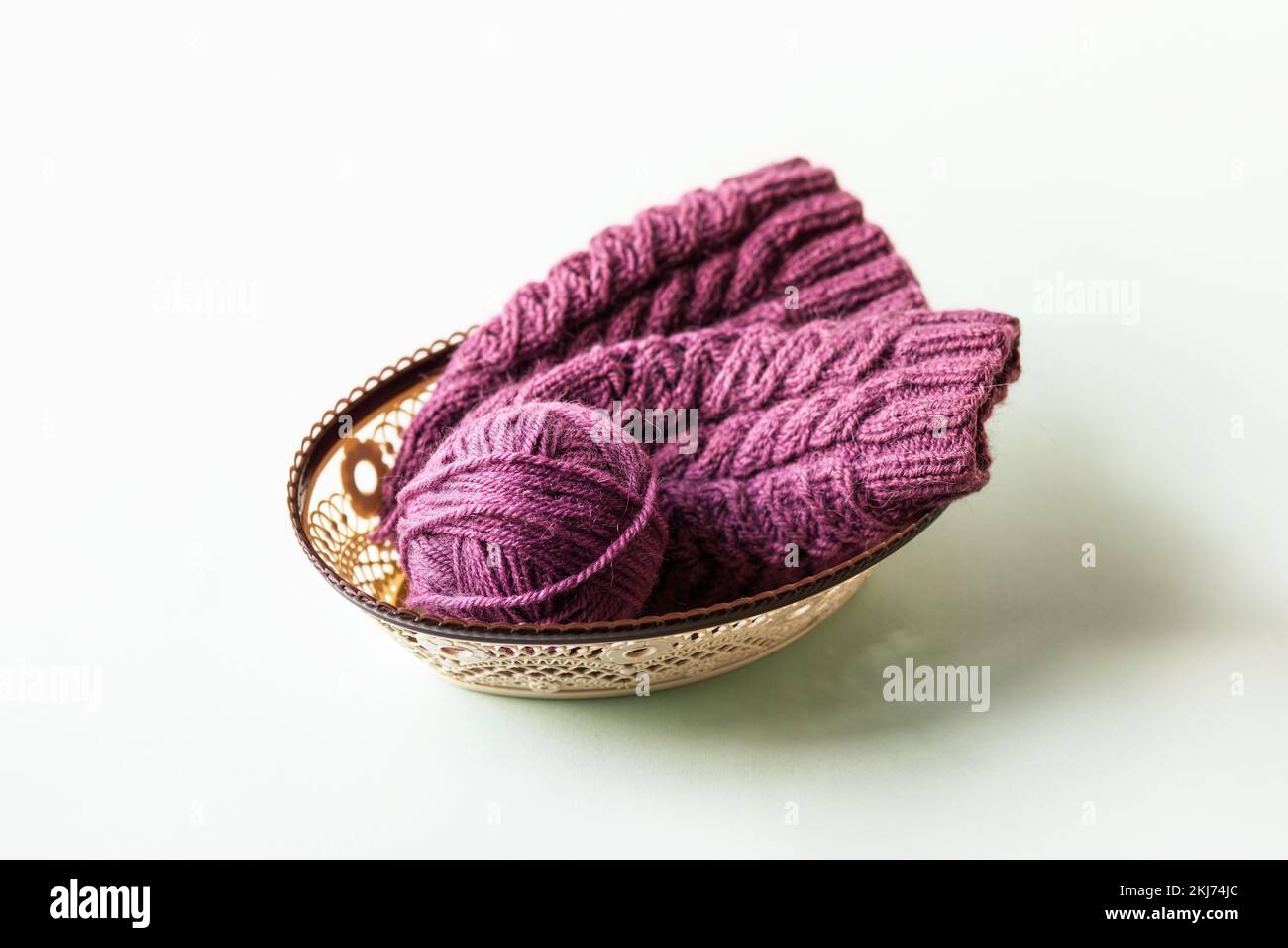 Una palla viola di filo e un cappello a maglia in un cesto su sfondo verde, hobby di lavorazione a maglia Foto Stock