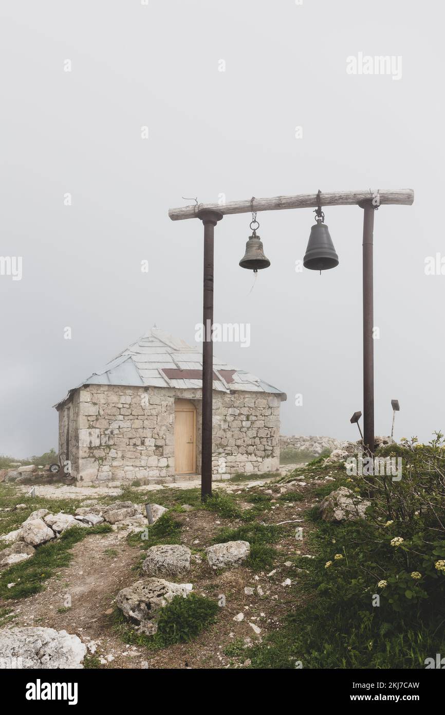 Antica chiesa ortodossa di San Giorgi in pietra a Khvamli catena montuosa in Georgia con campanile in legno semplice con due campane, tempo nebbia. Foto Stock