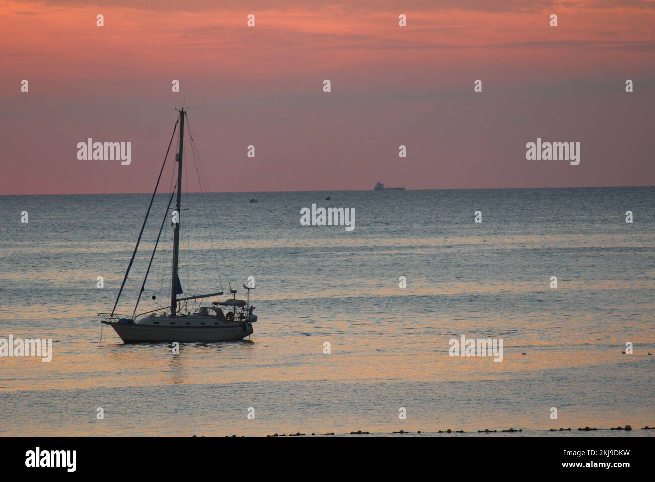 Silhouette di una barca a vela che galleggia pacificamente nella baia di Gorliz Plentzia (Paesi Baschi), con mare calmo, orizzonte e cielo rossastro di un tramonto Foto Stock