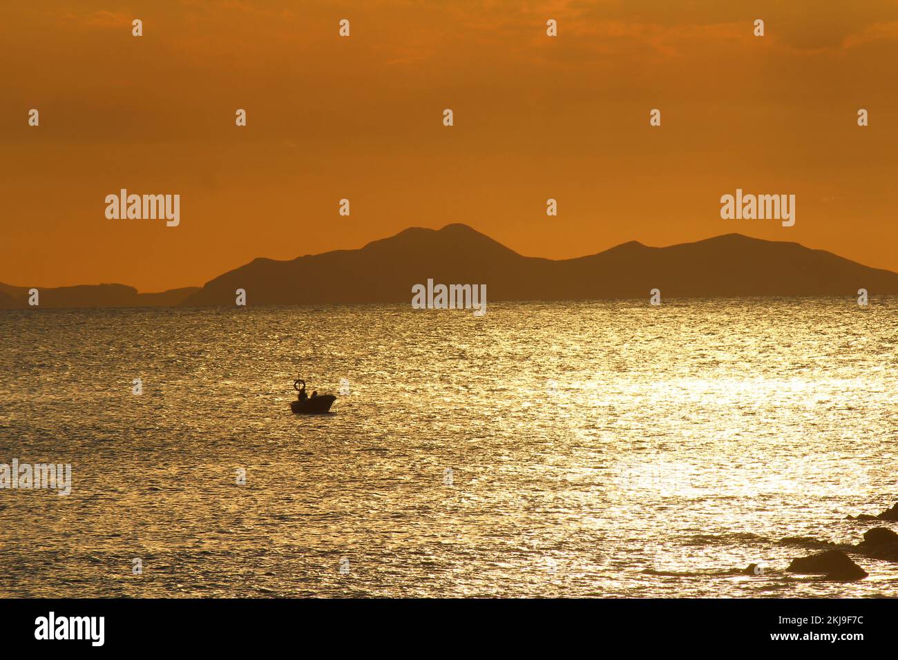 Tramonto in mare, caratterizzato dalla silhouette di una piccola barca che galleggia nei riflessi del sole, con montagne cantabriche sullo sfondo, viste da Gorliz Foto Stock
