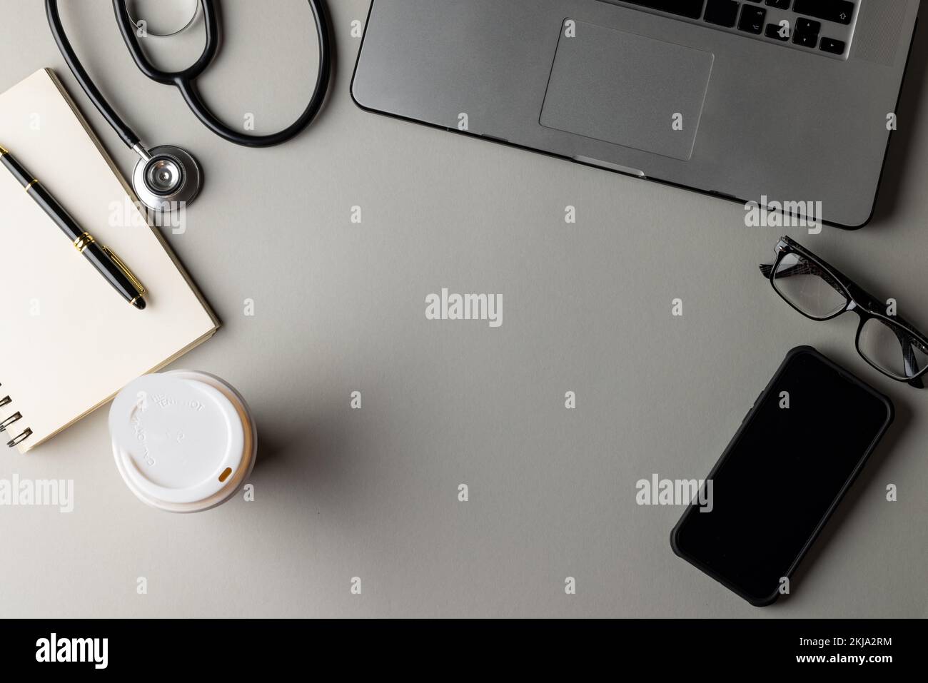 Stetoscopio, computer portatile, notebook, occhiali, smartphone e caffè su sfondo grigio con spazio copia Foto Stock