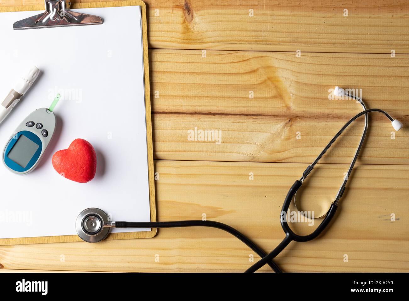 Stetoscopio e clipboard con glucometro e cuore rosso su fondo in legno con spazio copia Foto Stock
