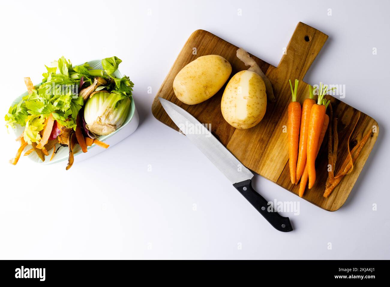Testa di coltello e verdure sul tagliere con scarti vegetali in cucina compostaggio bidone Foto Stock