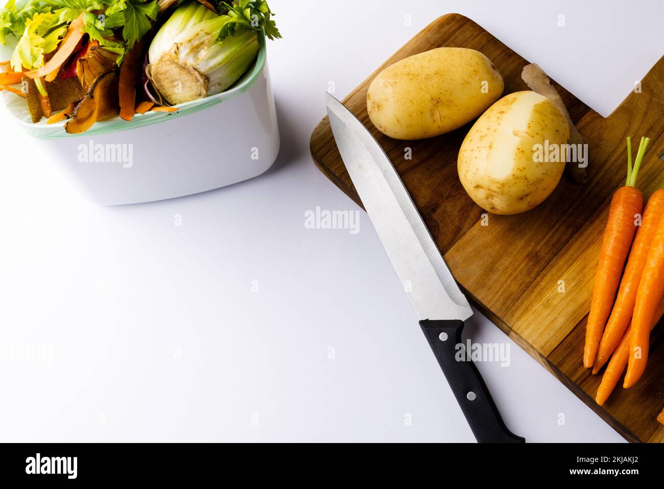 Coltello e verdure sul tagliere con scarti vegetali nel contenitore di compostaggio della cucina Foto Stock