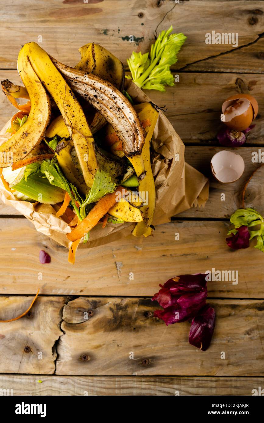 Overhead verticale di frutta biologica e scarti vegetali che si versano dal contenitore di compostaggio cucina completa Foto Stock
