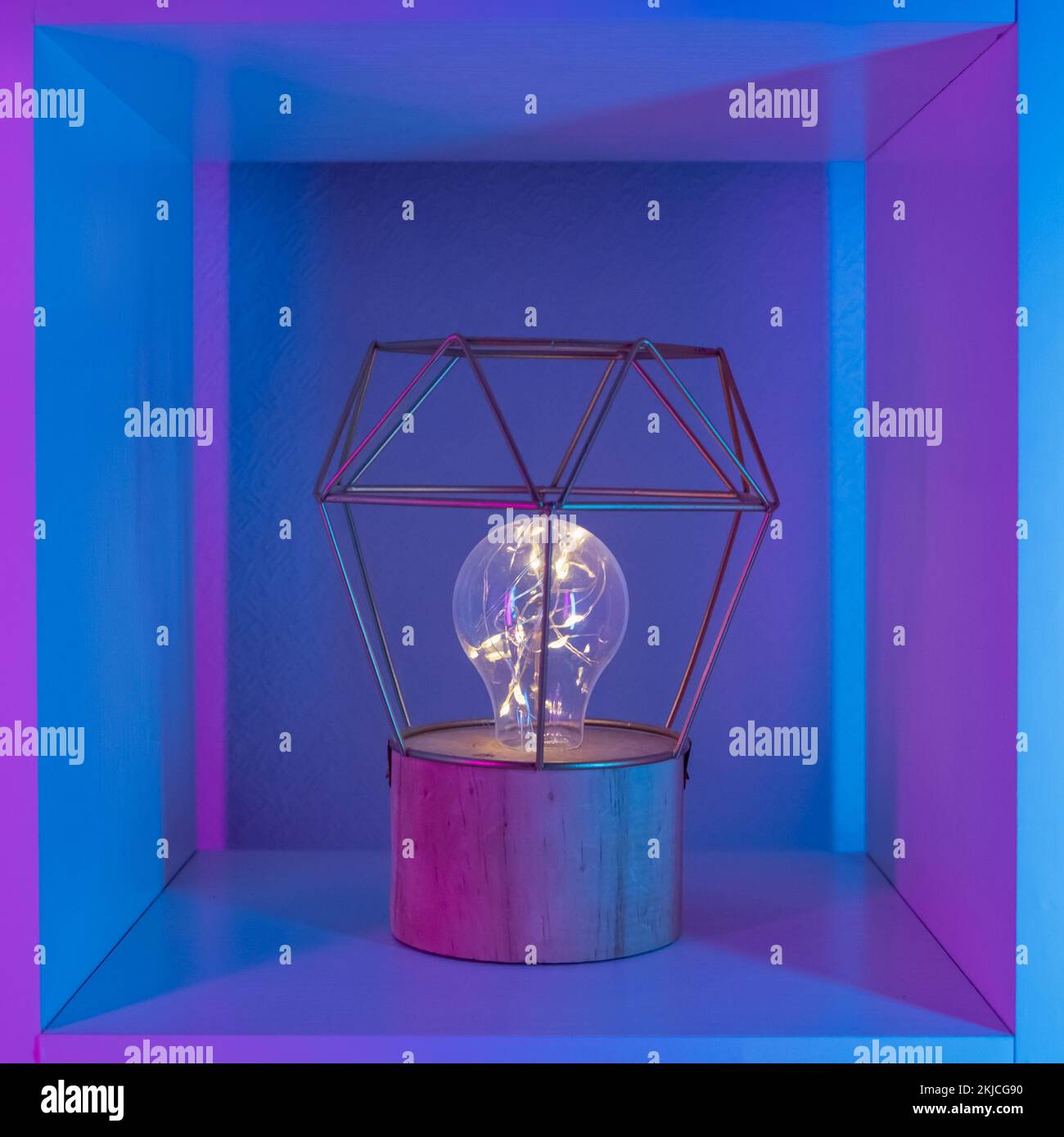 Lampada con paralume geometrico oro metallizzato su piedistallo in legno con lampada LED al neon in rack bianco. Foto Stock