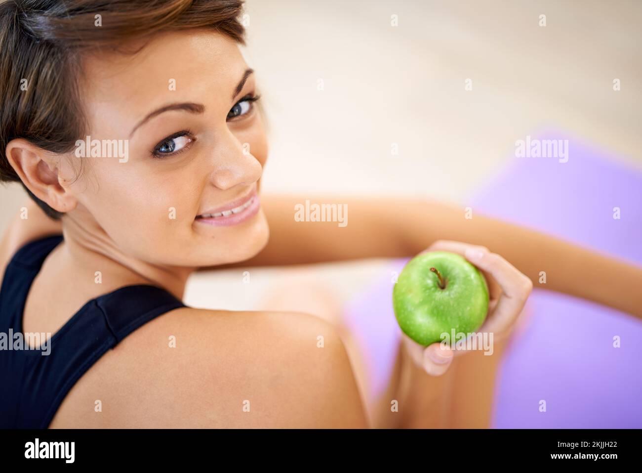 La sua arma segreta per una vita sana. una giovane donna sportiva seduta sul pavimento di una palestra che mangia una mela. Foto Stock