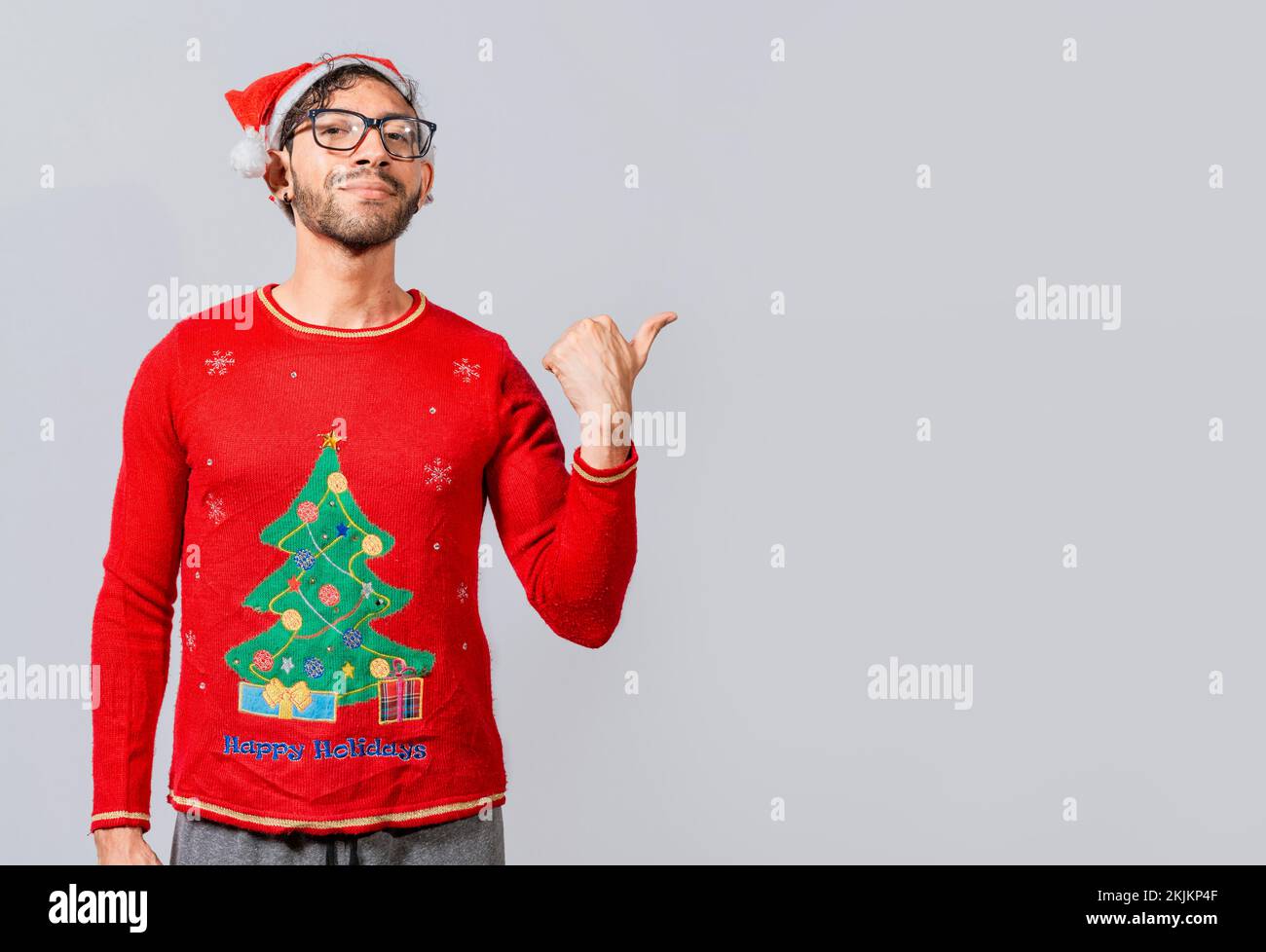 Amichevole uomo di Natale che indica uno spazio al lato. Giovane sorridente amichevole nei vestiti di natale che indica un promo. Allegro uomo di natale co Foto Stock