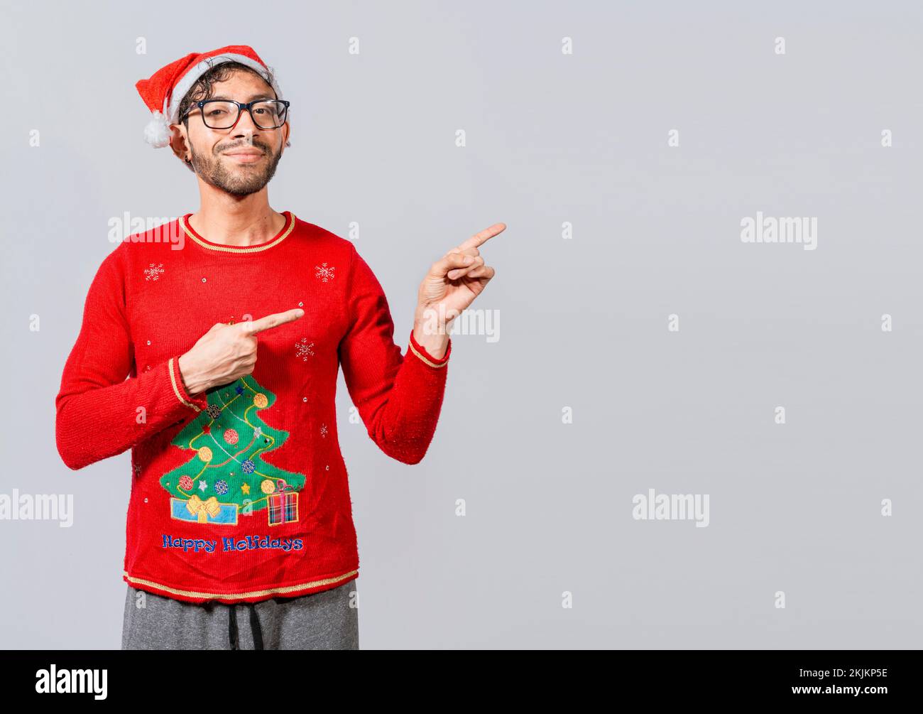 Allegro concetto di uomo di natale che punta promo offerta isolato, amichevole uomo di Natale che punta ad uno spazio al lato. Giovane amichevole sorridente in ch Foto Stock