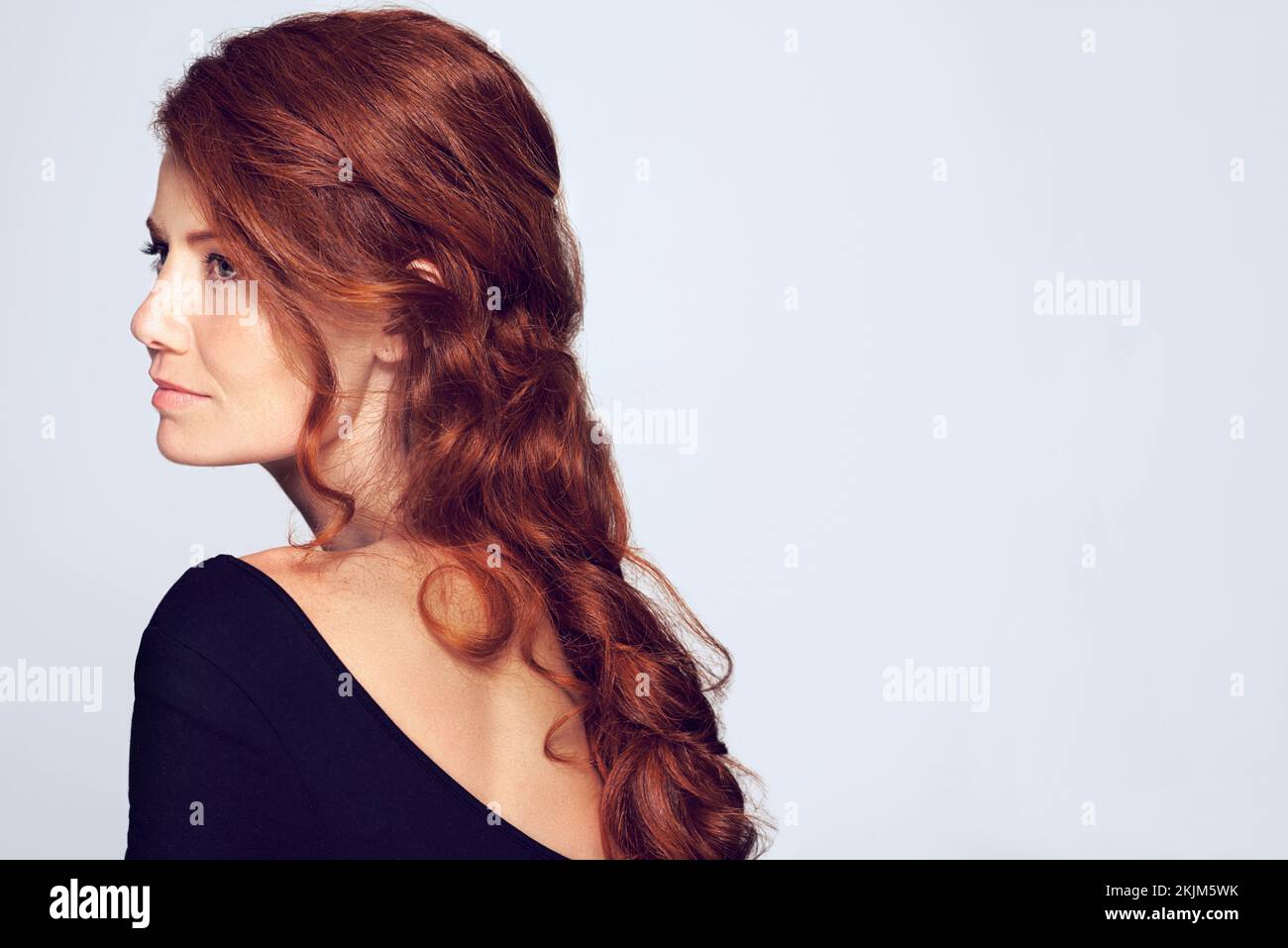 Ricci a cascata giù la schiena. Studio shot di una giovane donna con bei capelli rossi che si posano su uno sfondo grigio. Foto Stock