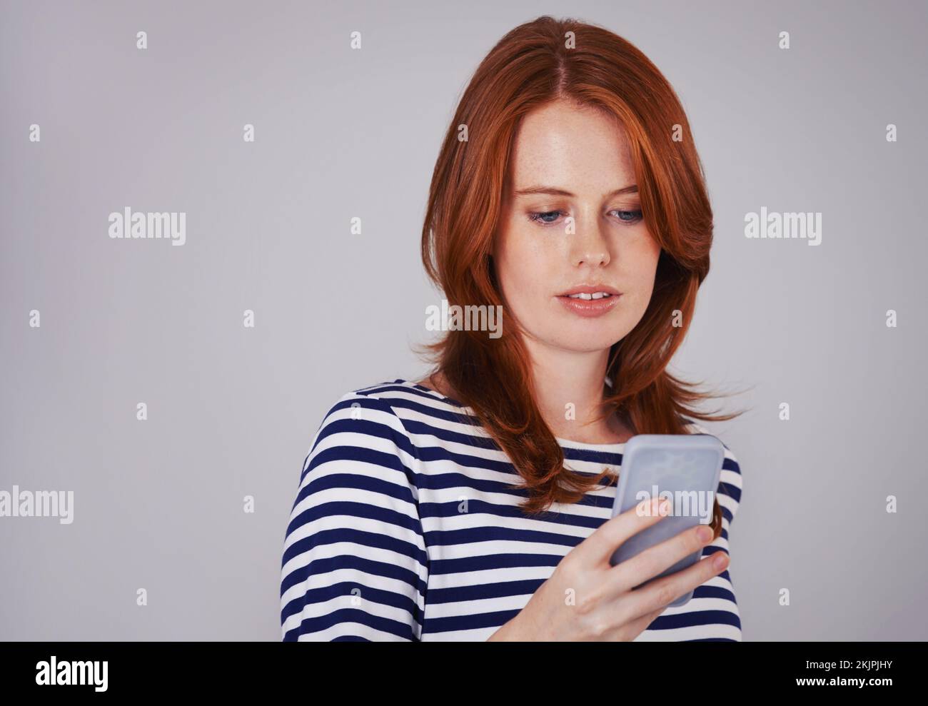 Dedicare del tempo al testo. Studio shot di una bella con capelli rossi inviare un testo sul suo telefono cellulare. Foto Stock