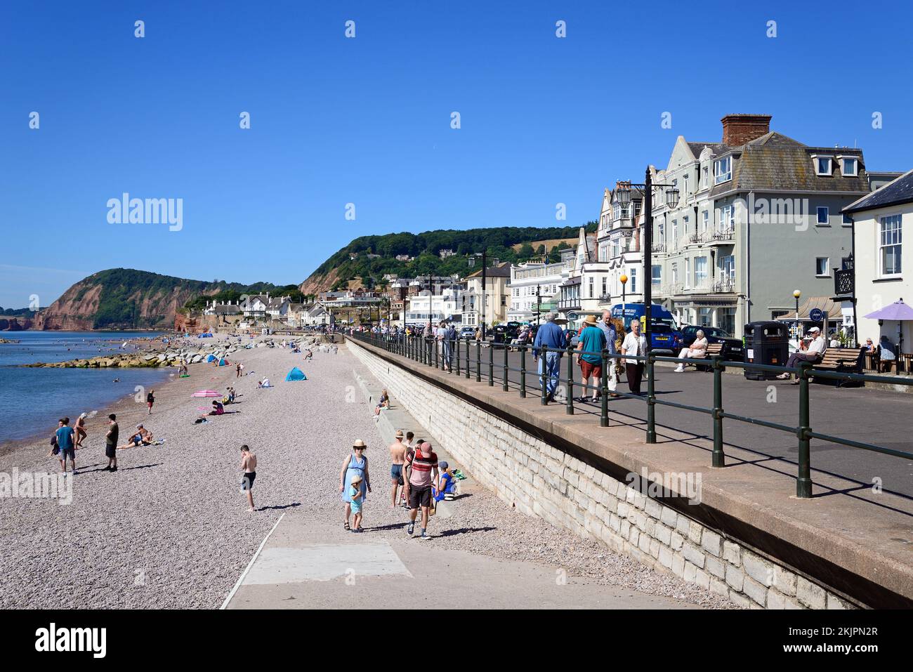 Turisti che si rilassano sulla spiaggia e sul lungomare con hotel che si affacciano sul mare, Sidmouth, Devon, Regno Unito, Europa. Foto Stock