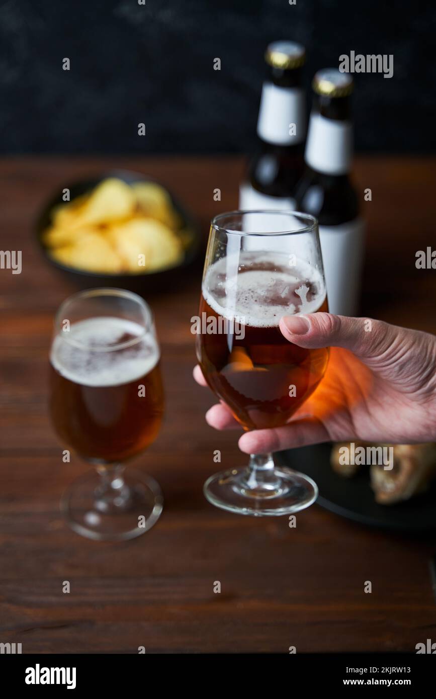 Due bicchieri con birra, spuntini e bottiglie su un tavolo di legno. Foto Stock