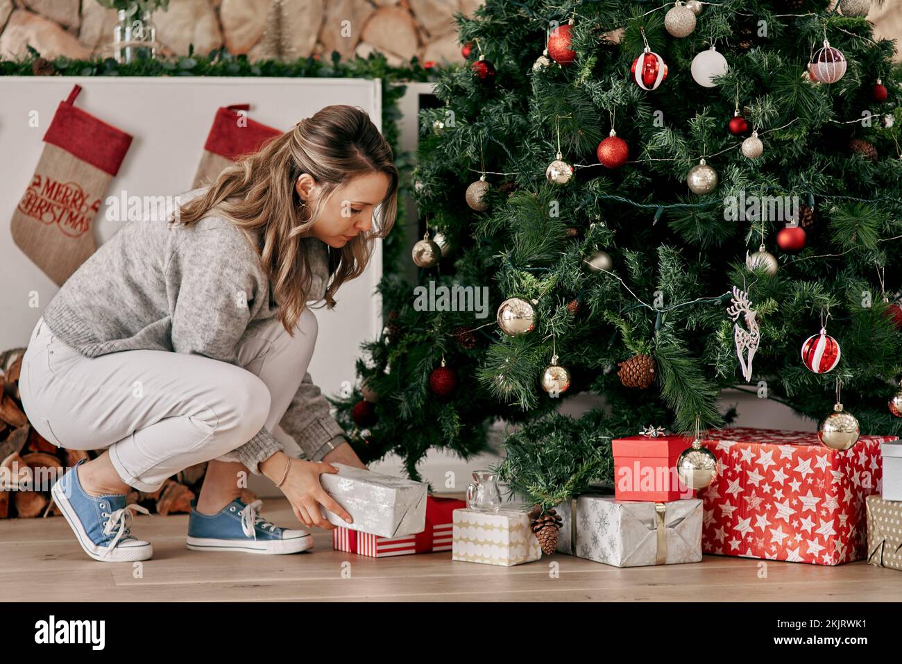 Natale, regalo di albero e festa con la donna, decorazione, scatola di festa e tradizione a casa di famiglia. Regali sotto l'albero di Natale Foto Stock