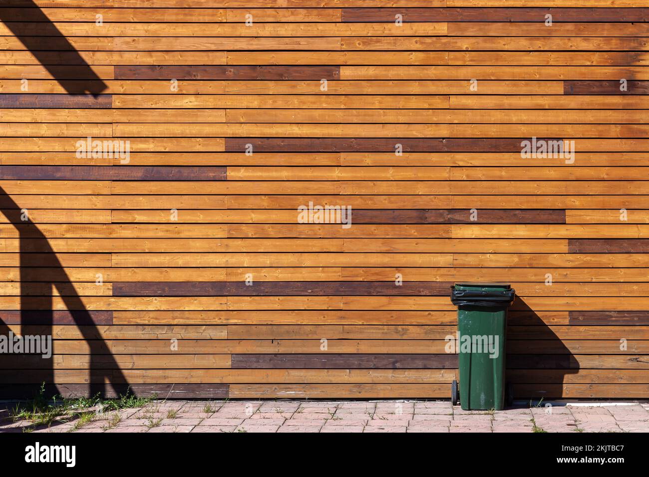 Cestino verde si trova vicino a una parete di legno in una giornata di sole Foto Stock
