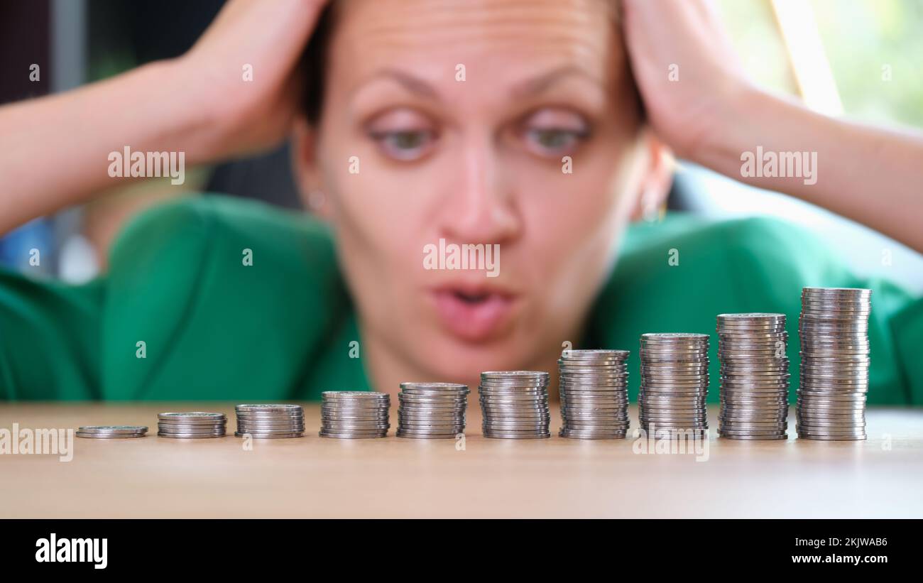 Donna scioccata che guarda mucchi di monete e che tiene in testa Foto Stock