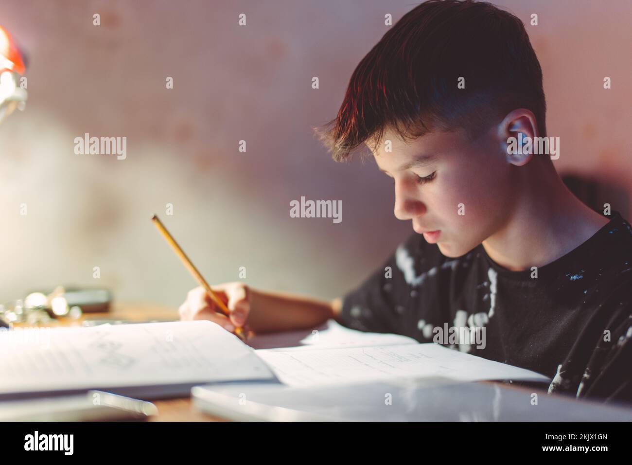 Giovane ragazzo caucasico diligente che pensa mentre fa i compiti a casa di sera Foto Stock