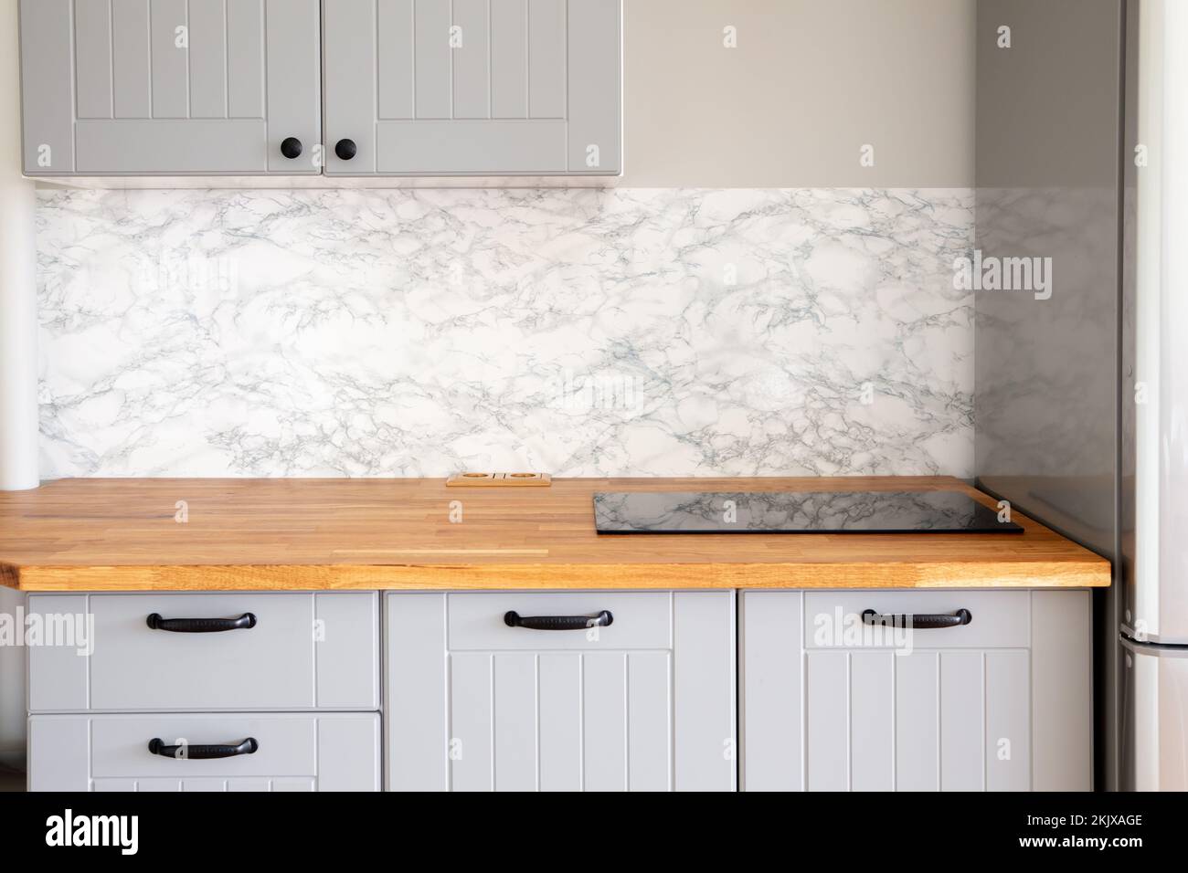 Vuoto moderno minimal grigio cucina, muro di marmo, massello di legno naturale macellaio blocco piano con costruito in piccola stufa, manici neri. Foto Stock