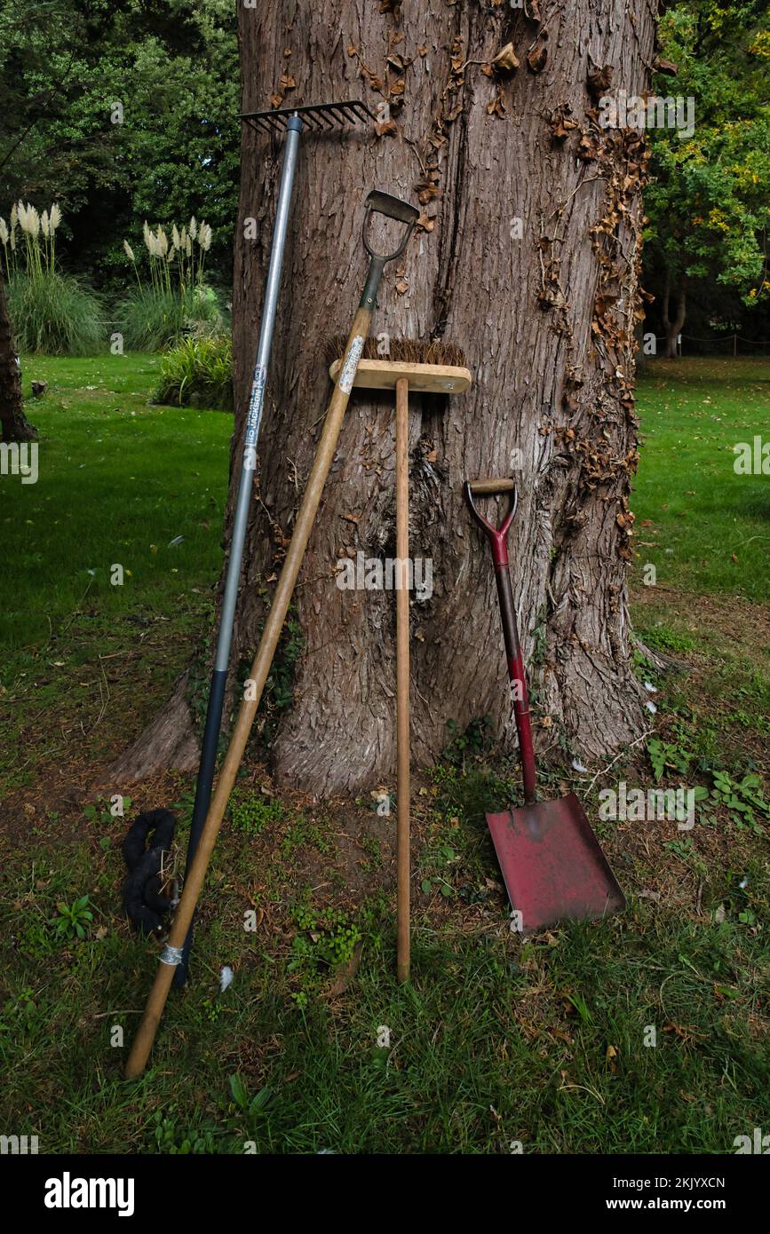 Pausa tè giardinieri e appendere degli attrezzi da giardino, spike, rake hoe e pennello propped up contro un albero. Foto Stock