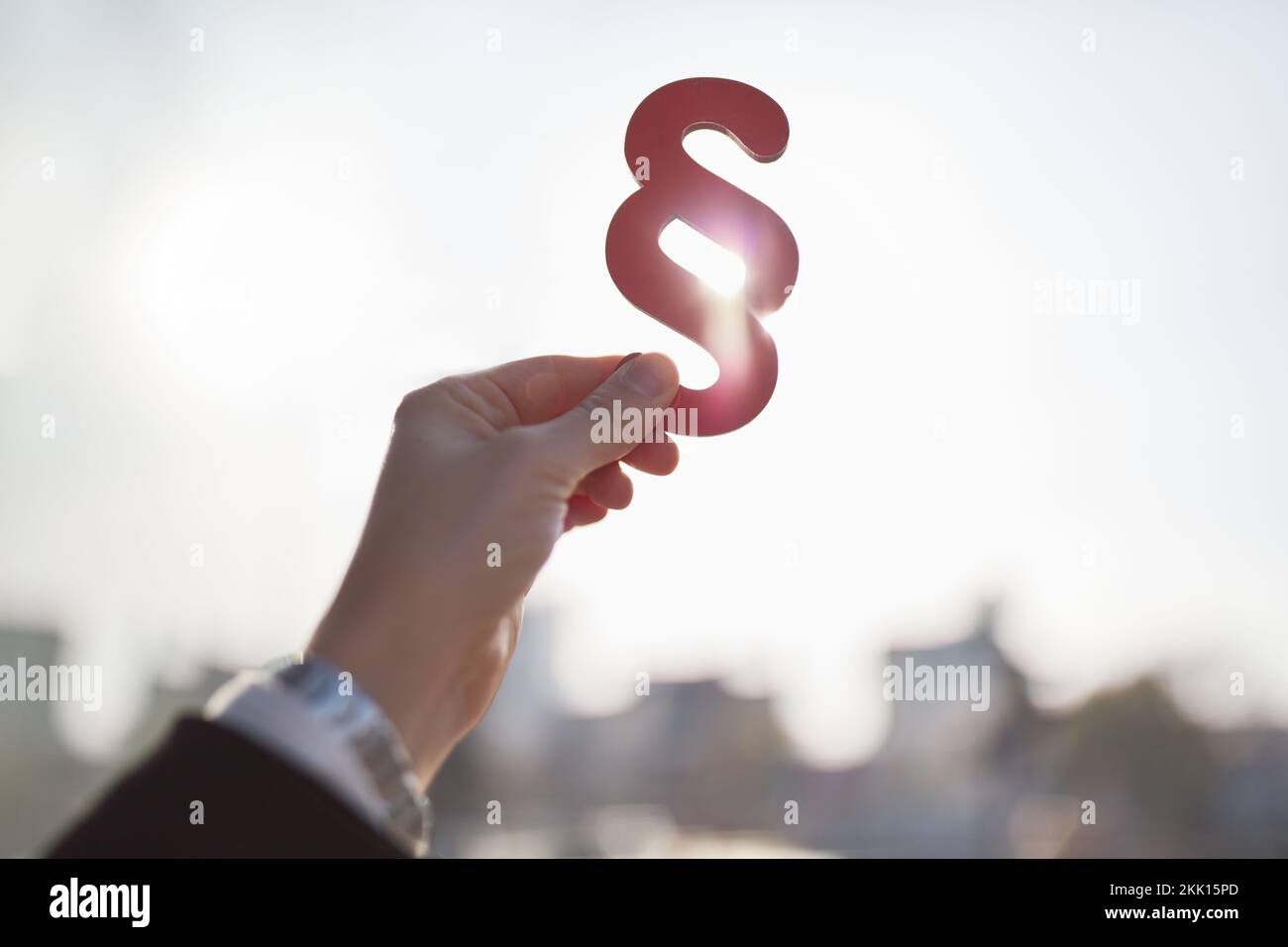 Mano che tiene grande segno rosso di paragrafo contro il sole come simbolo di concetto di legge Foto Stock
