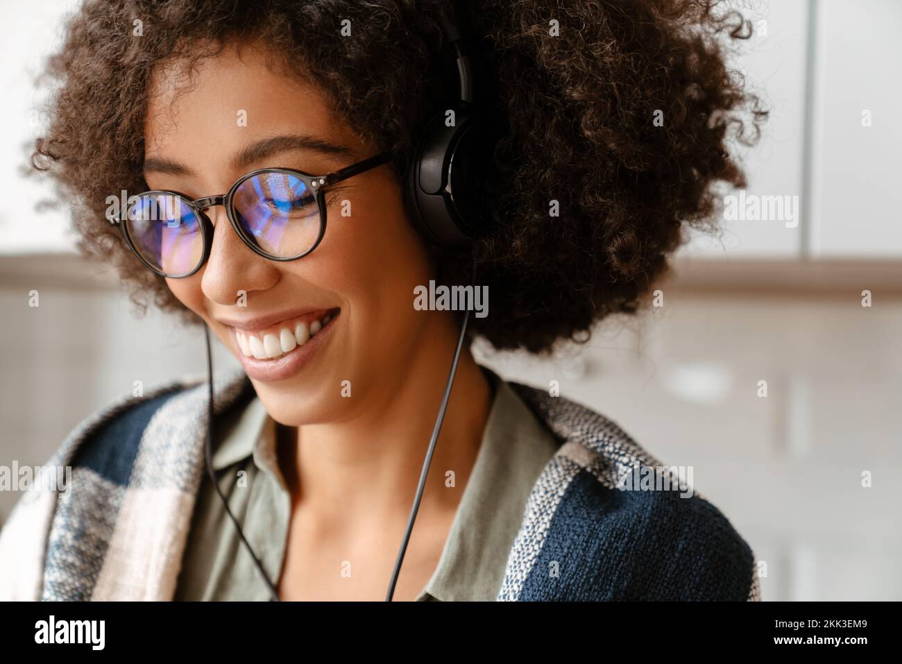 Giovane donna afroamericana con capelli ricci e occhiali che utilizzano gli auricolari a casa Foto Stock