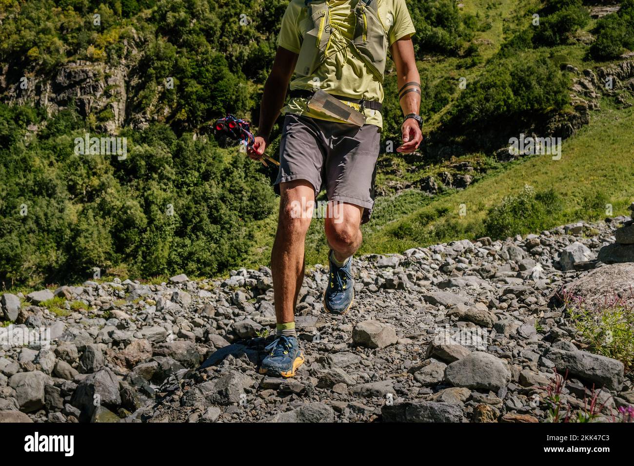corridore maschio con pali da trekking che corrono su rocce Foto Stock