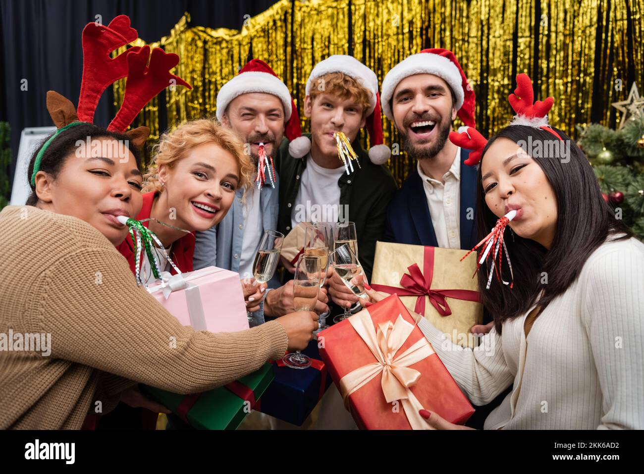 Uomini d'affari multiculturali con corna da festa in regalo e champagne da clinking durante la festa aziendale di Capodanno Foto Stock