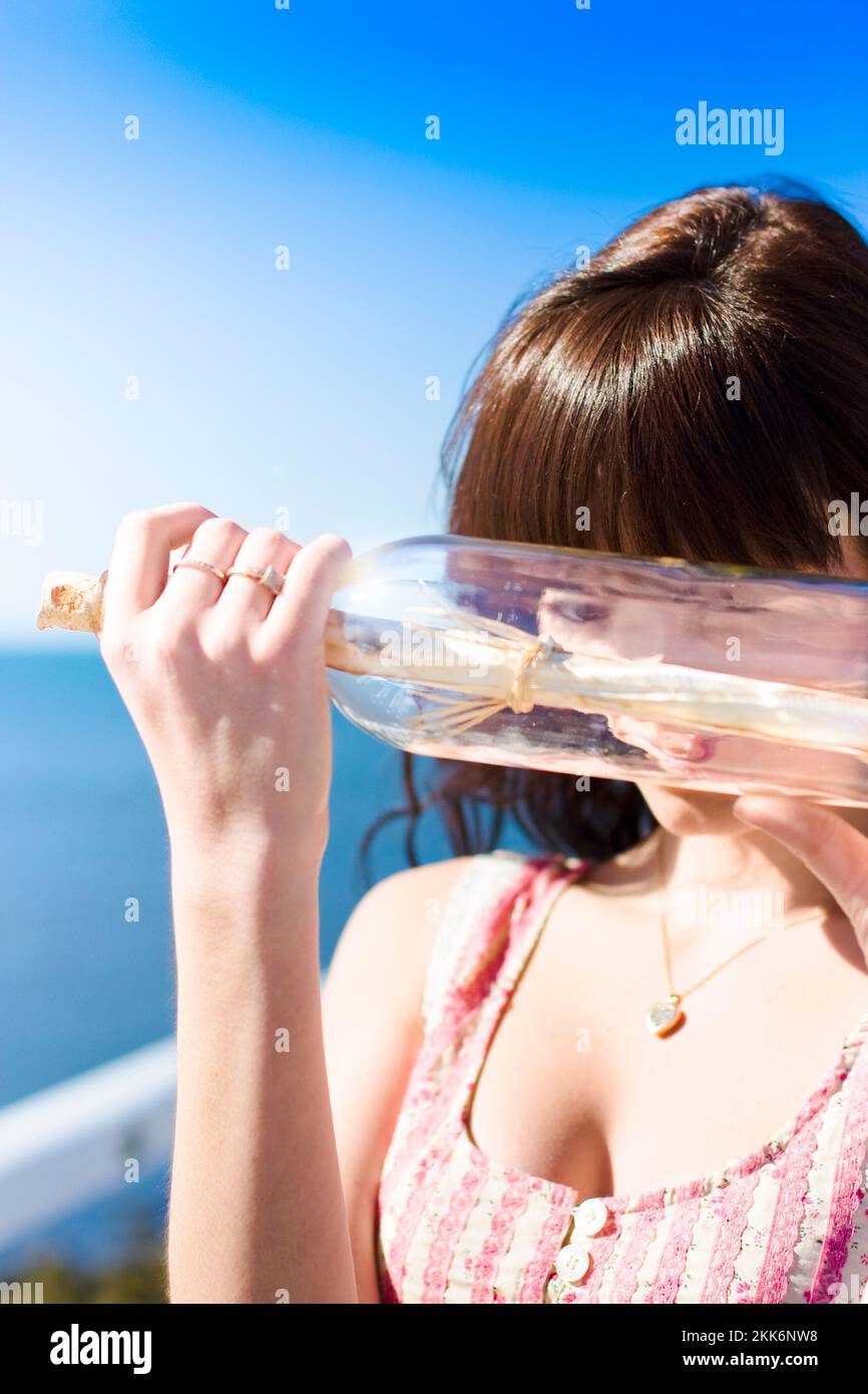 Una donna guarda attraverso il vetro di un messaggio in bottiglia trovato lavato fino dalla marea dell'oceano Foto Stock