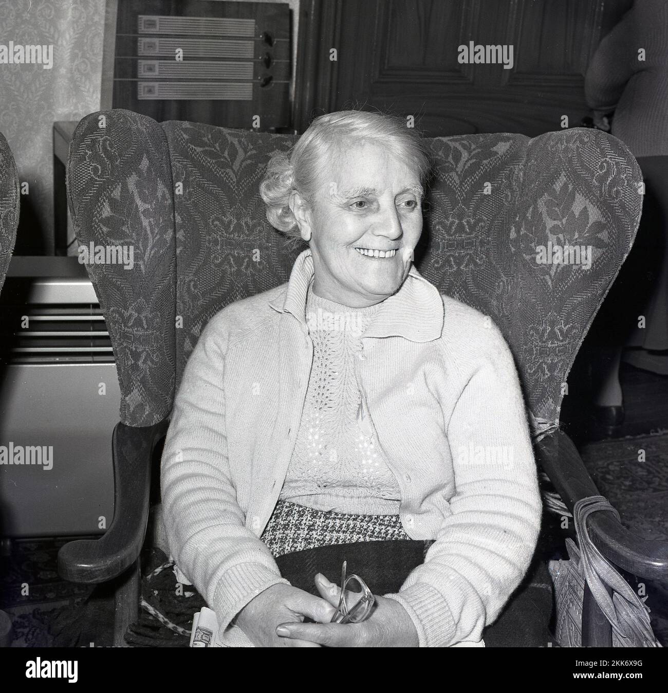 1965, storica, felice anziana donna seduta su una sedia in una casa di anziani, Inghilterra, Regno Unito. Foto Stock