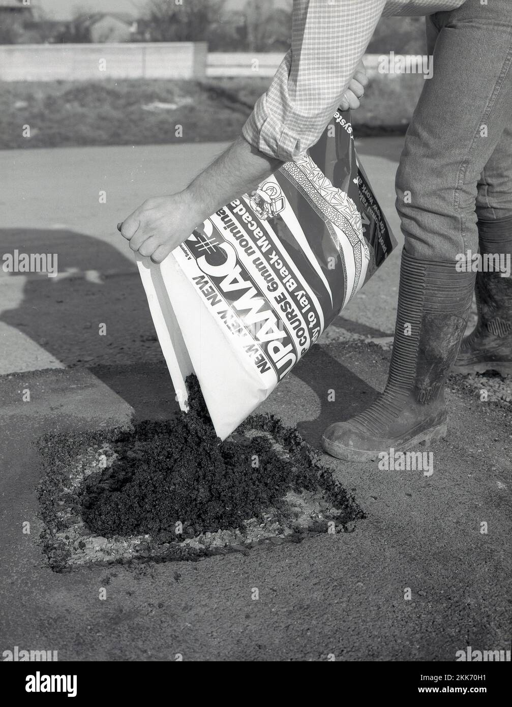 1980s, rifacing, un uomo che utilizza un sacchetto di un nuovo prodotto da costruzione per riparare o riparare un vialetto, un preparato-mix o pronto per posare tarmacadam nero o asfalto, noto come un catrame a freddo, Inghilterra, Regno Unito. Foto Stock
