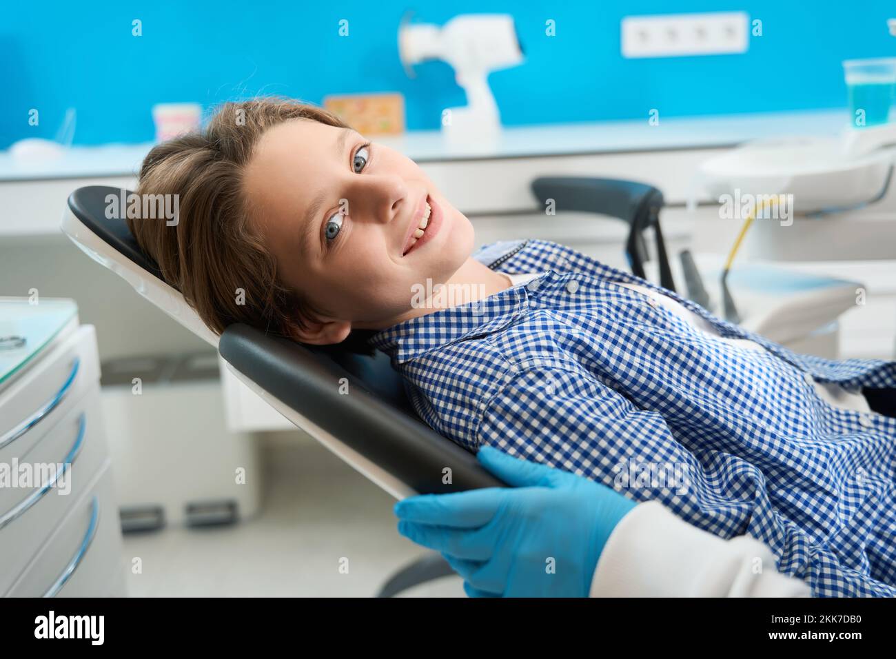 Sorridente adolescente si siede in una sedia dentale tra attrezzature speciali Foto Stock