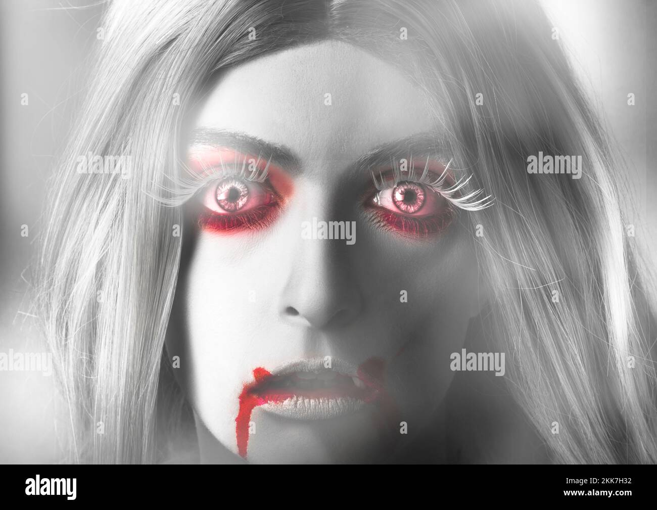 Spooky primo piano ritratto sul volto di una bella ragazza vampiro bionda che guarda fuori con un'espressione spaventosa di shock horror con sangue sparato rosso ey Foto Stock