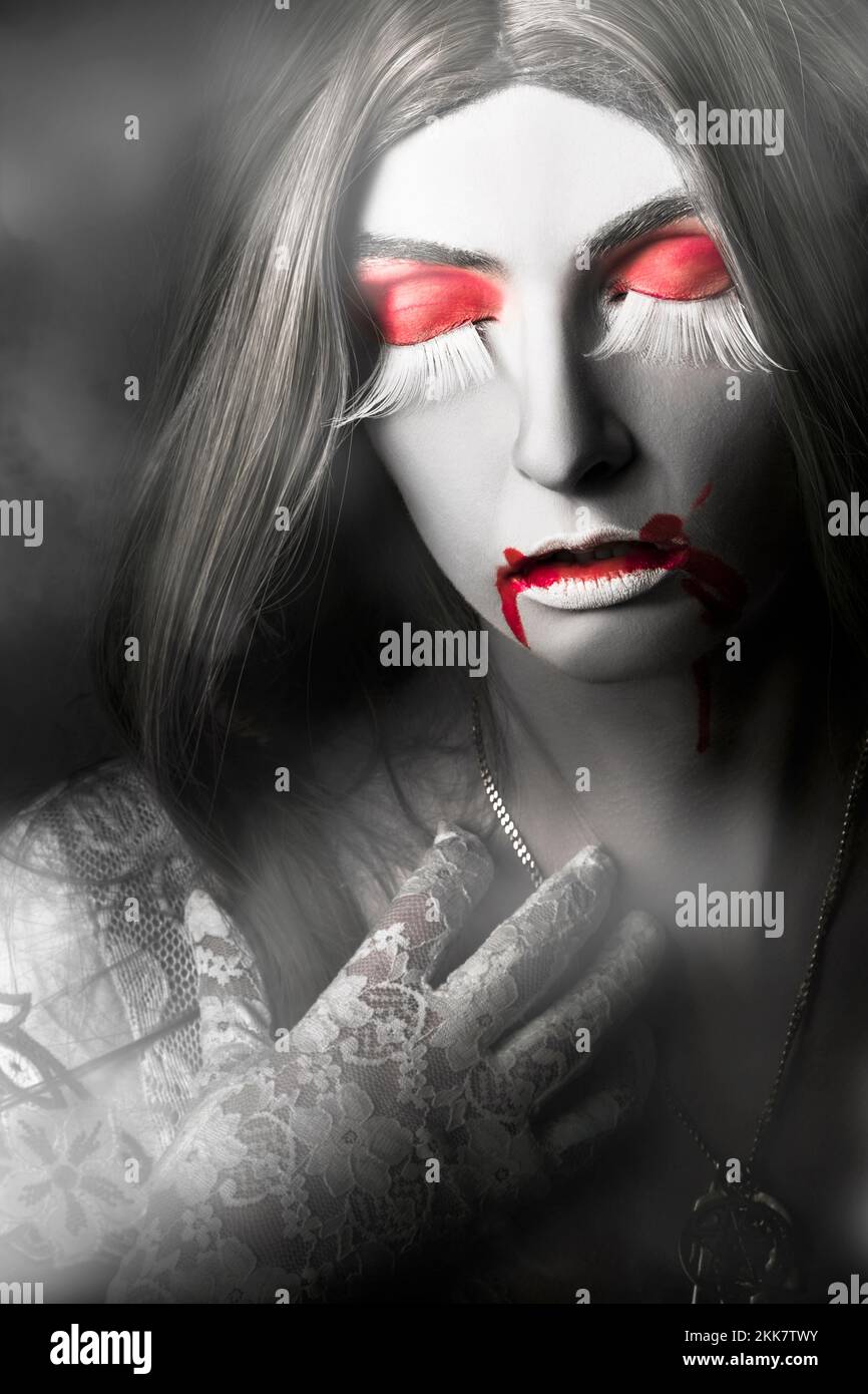 Halloween ritratto di una bella donna giovane vampiro con sangue le labbra rosse indossano un abito in pizzo bianco che raggiunge la collana d'argento con espressione di grie Foto Stock