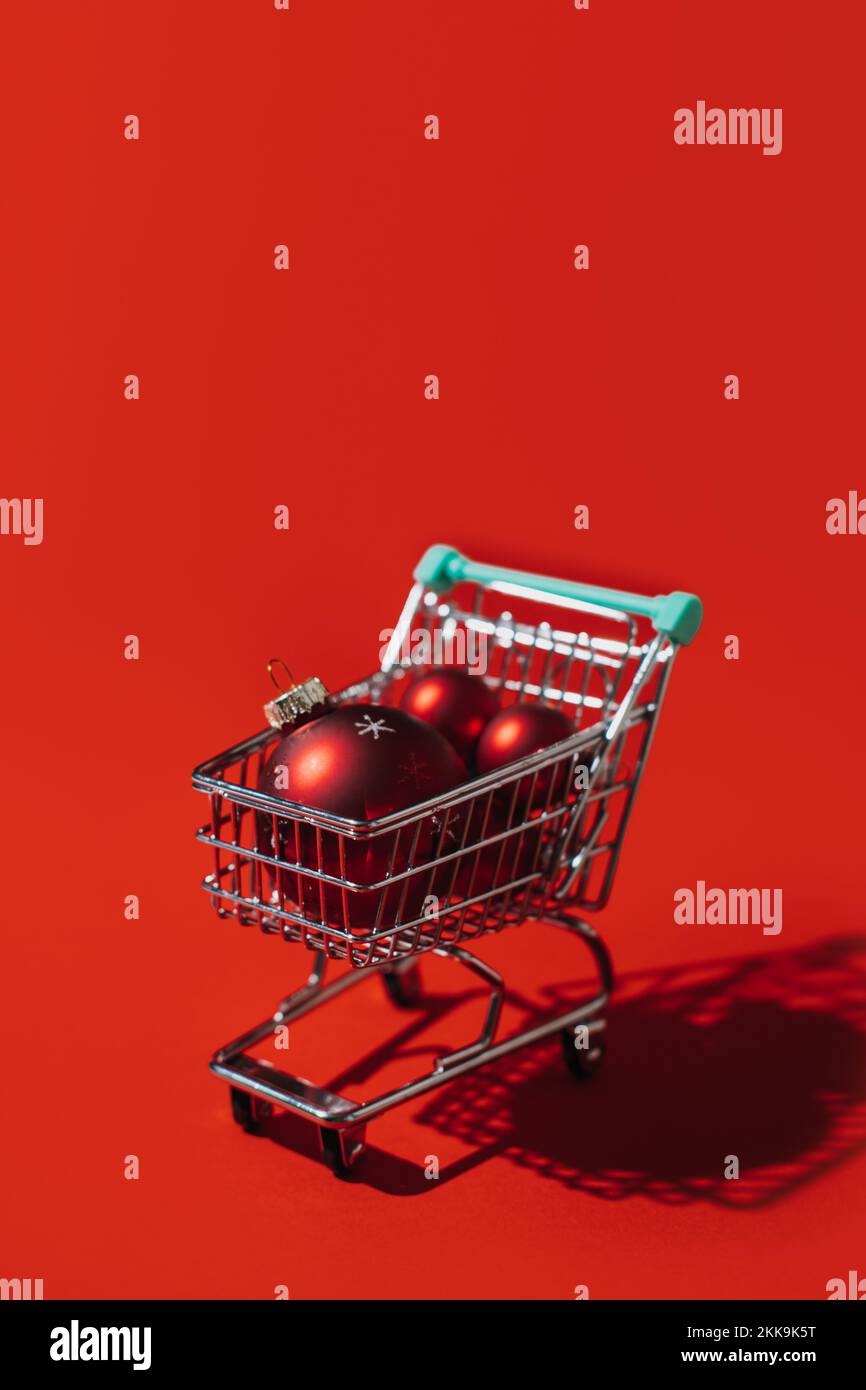 Carrello di Natale con palle ornamentali rosse di Natale su sfondo rosso. Minimal Natale shopping vendita banner web copia concetto di spazio. Foto Stock