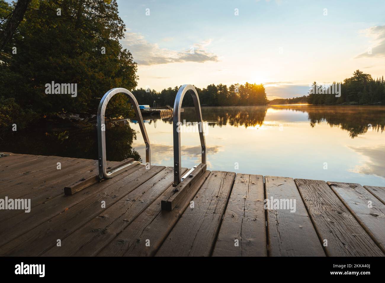 Il sole sorge su un molo su un lago tranquillo Foto Stock